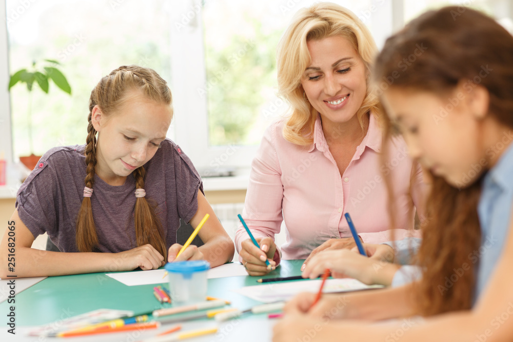 Pupils and teacher sitting at desk and drawing by them in album. Pupils and teacher sitting at desk and drawing by them in album.