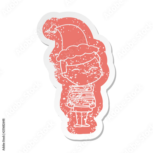 cartoon distressed sticker of a smiling boy with stack of books wearing santa hat