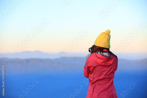 Woman tourist wearing vivid jacket  hold camera shoot mountain view during twilight time
