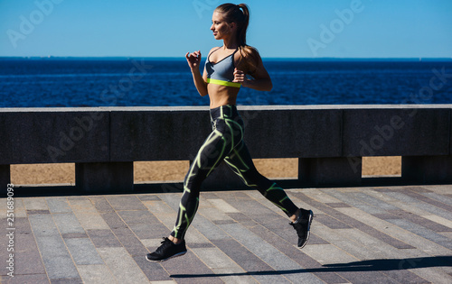 Young sexy girl model runs in the city on the embankment in the morning. Workout fitness healthy lifestyle concept