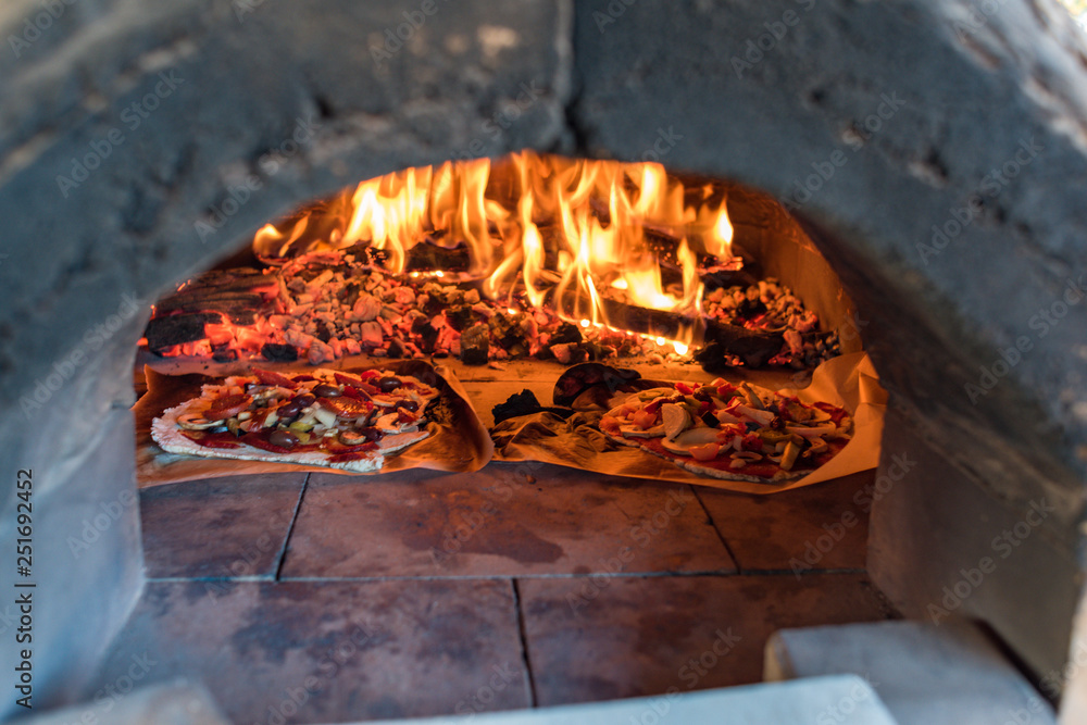 Italian pizza cooking in pizza oven over open flame