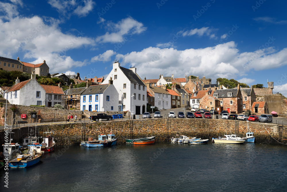 Boats moored at stone pier in Crail Harbour with Crail House lookout turret over the North Sea in Fife Scotland UK