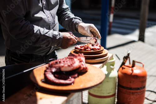 A man cooks Galician octopus in a street stall. Man is cutting the octopus and placing it on a wooden plate. photo