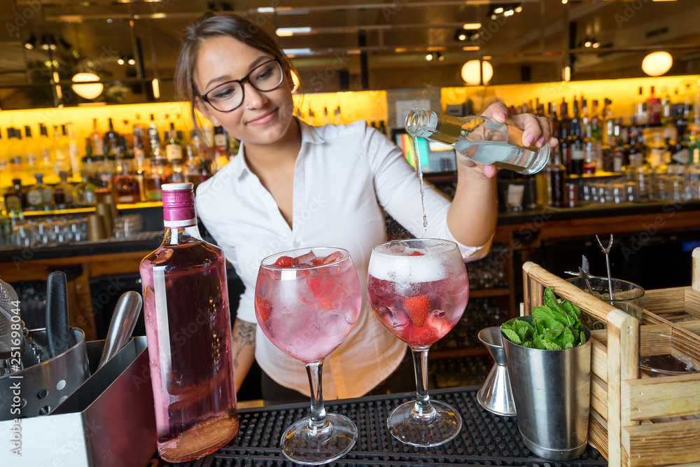 female beautiful smart bartender mixologist bar person makes prepares gin tonic cocktail drink pink mint fish bowl glass