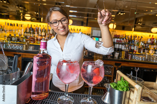 female beautiful smart bartender mixologist bar person makes prepares gin tonic cocktail drink pink mint fish bowl glass