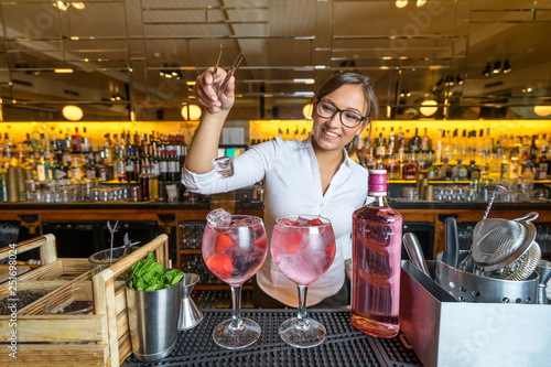 Obraz na płótnie female beautiful smart bartender mixologist bar person makes prepares gin tonic cocktail drink pink mint fish bowl glass w salonie