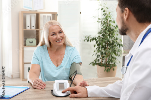 Doctor checking mature woman's pulse with medical device in hospital