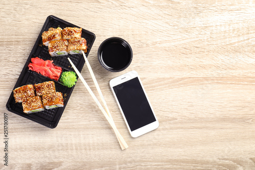 Flat lay composition with sushi rolls and smartphone on wooden table, space for text. Food delivery