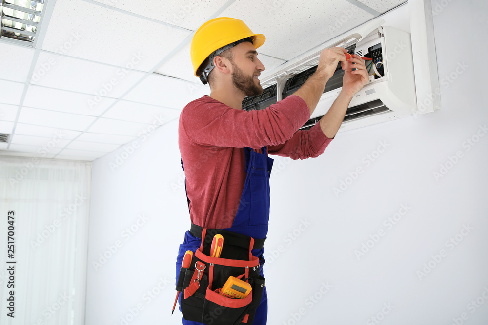 Electrician with screwdriver repairing air conditioner indoors Electrician with screwdriver repairing air conditioner indoors