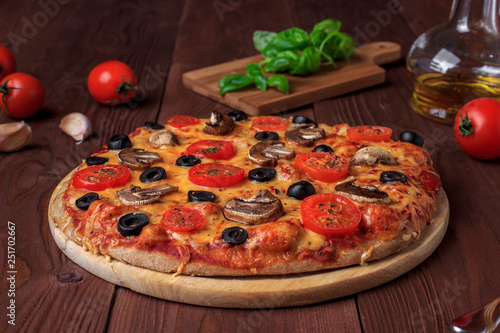 Traditional Italian vegetarian pizza with mushrooms, cherry tomatoes, black olives and basil on brown wooden table