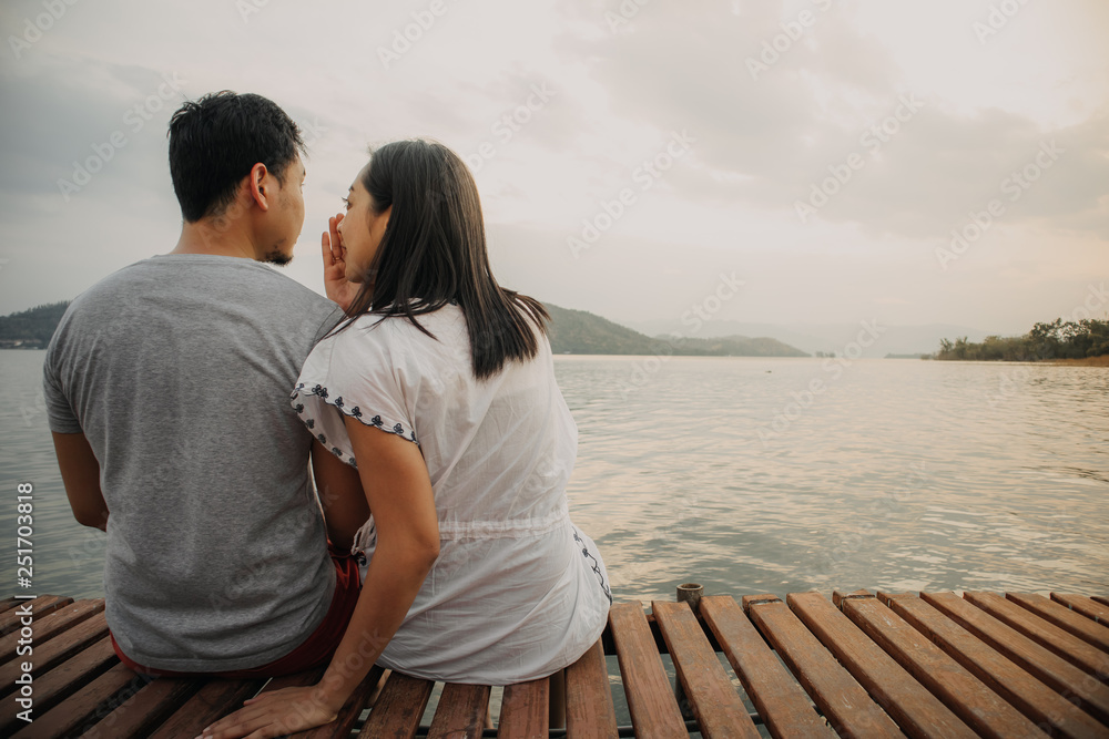 Romantic Asian couple whispering and enjoy the lake view.