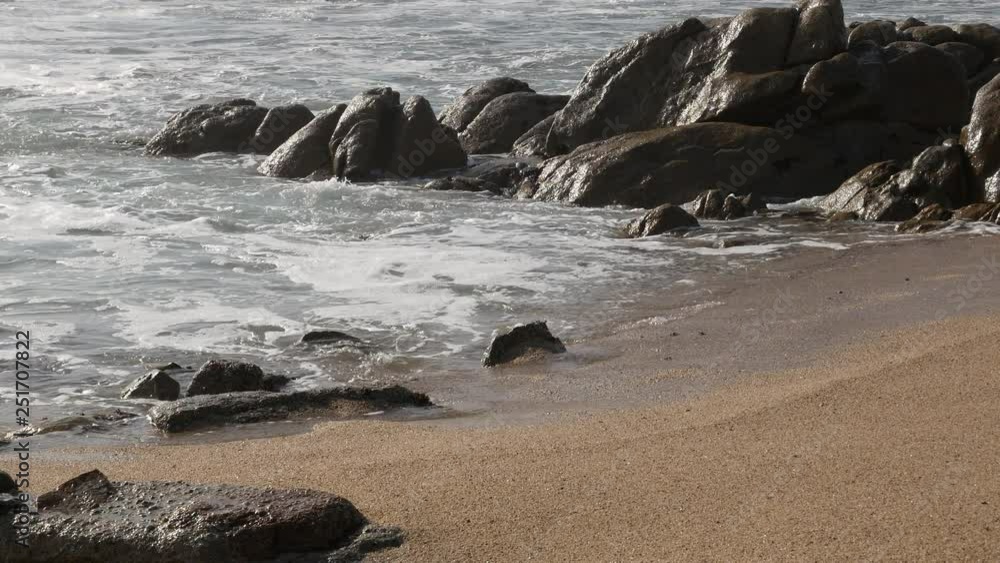 White foamy waves lap on the sandy beach with sandstone rocks in background White foamy waves lap on the sandy beach with sandstone rocks in background