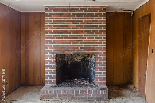 Red brick fireplace set against wood panel walls in an abandoned house