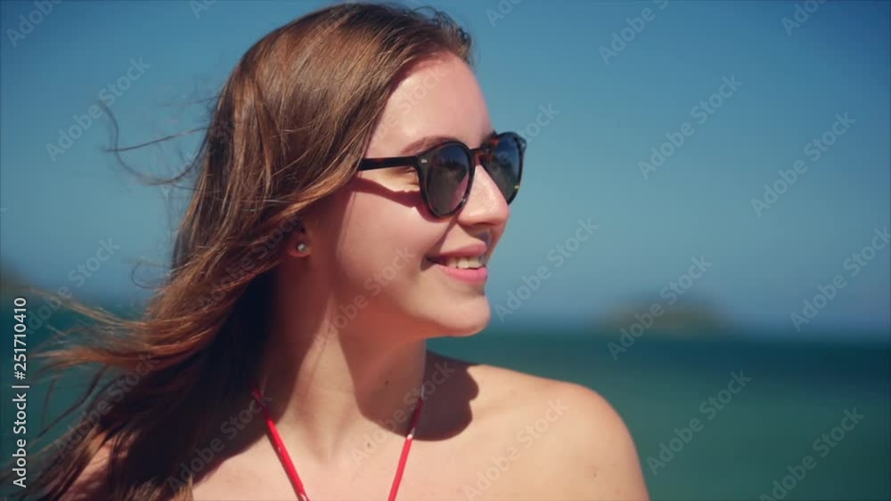 Close Up Portrait of European Beautiful Cute Brunette Young Woman or Cheerful Girl Smiling Looking at Camera, Running Hand Through Hair Blowing in Wind on Tropical Beach, Slow Motion. Close Up Portrait of European Beautiful Cute Brunette Young Woman or Cheerful Girl Smiling Looking at Camera, Running Hand Through Hair Blowing in Wind on Tropical Beach, Slow Motion.
