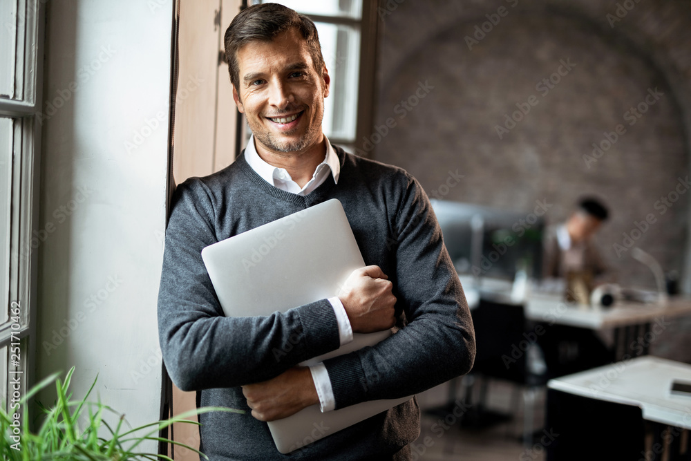 Portrait of happy businessman with laptop standing in the office. Portrait of happy businessman with laptop standing in the office.