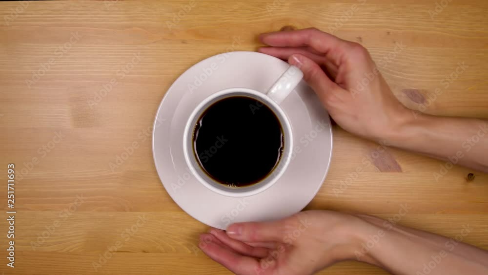 Female hand reaches in and picks up a cup of coffee and saucer from a wood table. Female hand reaches in and picks up a cup of coffee and saucer from a wood table.