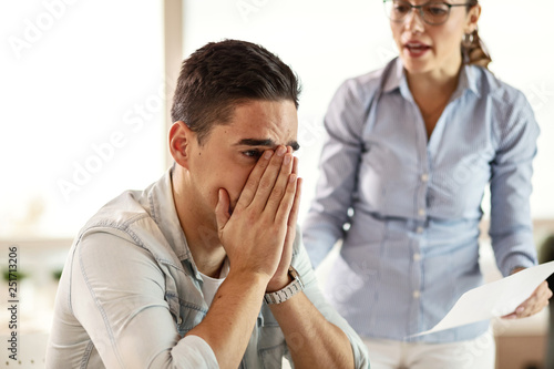 Young businessman feeling depressed while being criticized by bossy businesswoman.