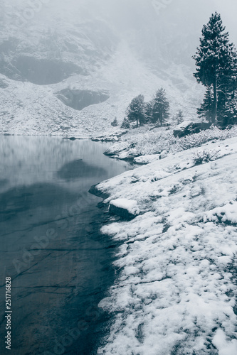 Winter lake, snow in coniferous forest on shore of mountain lake