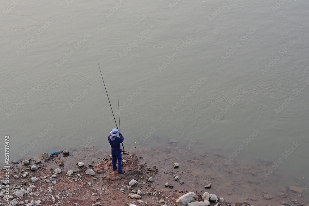 Angler is fishing /Men standing fishing in the river The background is gray water.