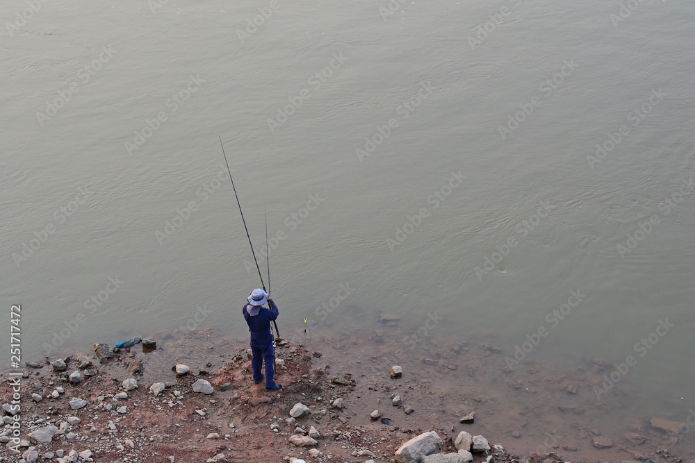Angler is fishing /Men standing fishing in the river The background is gray water. Angler is fishing /Men standing fishing in the river The background is gray water.