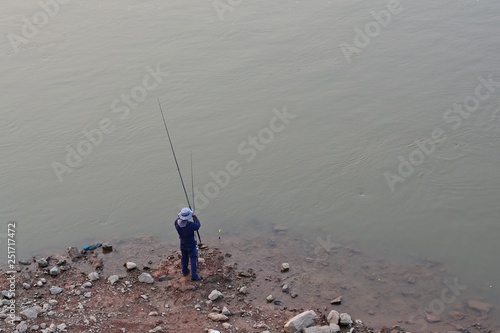 Angler is fishing /Men standing fishing in the river The background is gray water.