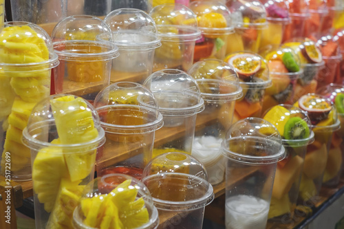 Street food vender selling blend fruit juice with fruits in clear plastic glass on display for customer to choose.