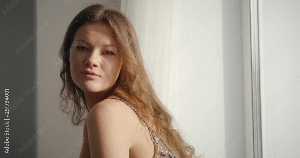 Portrait of a pretty brunette looking into the camera, smiles, she looks out the window and again into the camera. Portrait of a pretty brunette looking into the camera, smiles, she looks out the window and again into the camera.
