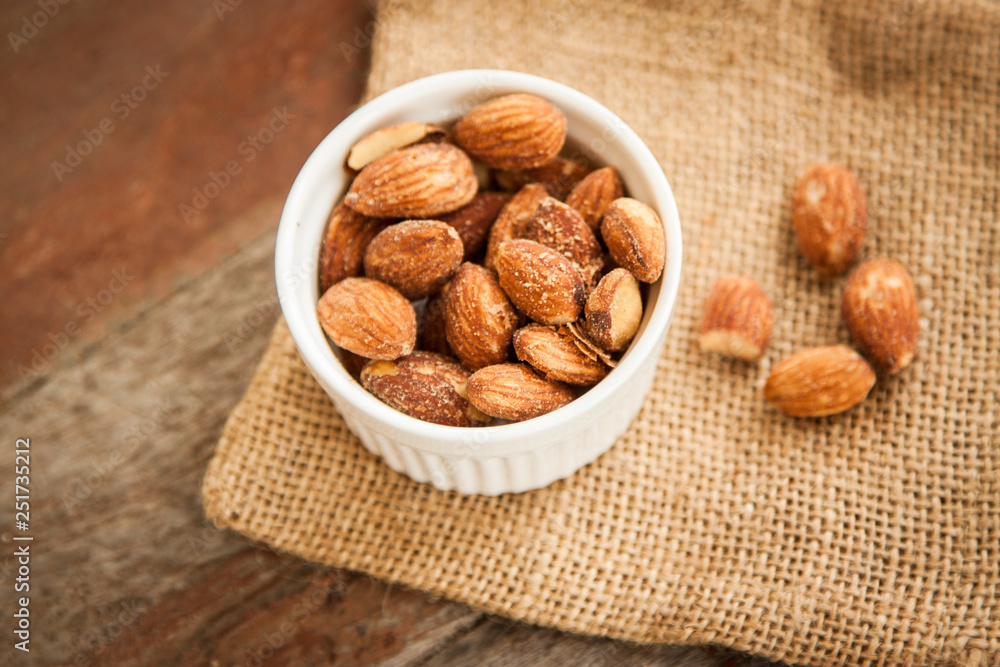Close up Almonds with salted and Roasted in the white cup put on the sackcloth and wood floor, the great snack Close up Almonds with salted and Roasted in the white cup put on the sackcloth and wood floor, the great snack