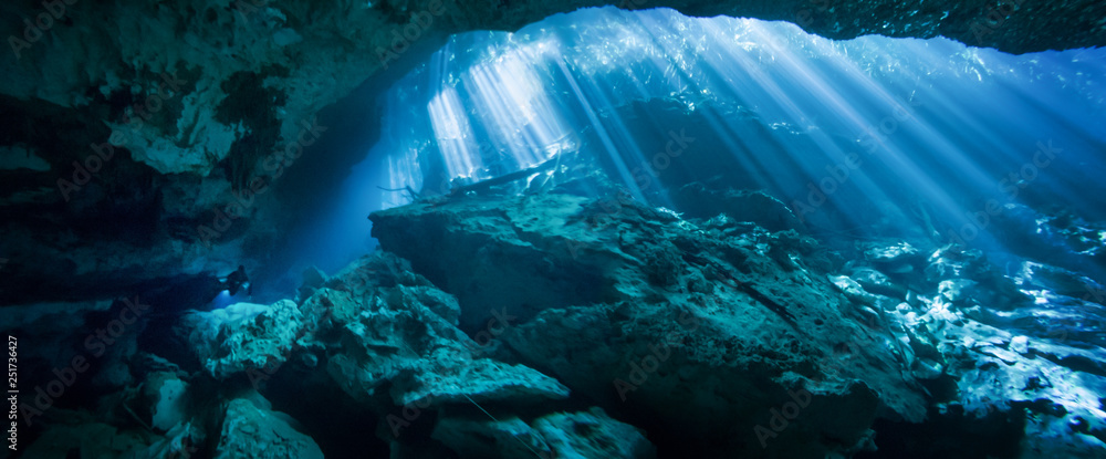 Sunlight shining through an opening in the El Jardin del Eden cenote with a scuba diver in the background. Sunlight shining through an opening in the El Jardin del Eden cenote with a scuba diver in the background.