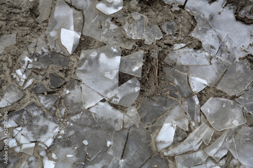 Textured surface of frozen cracked ice on muddy ground