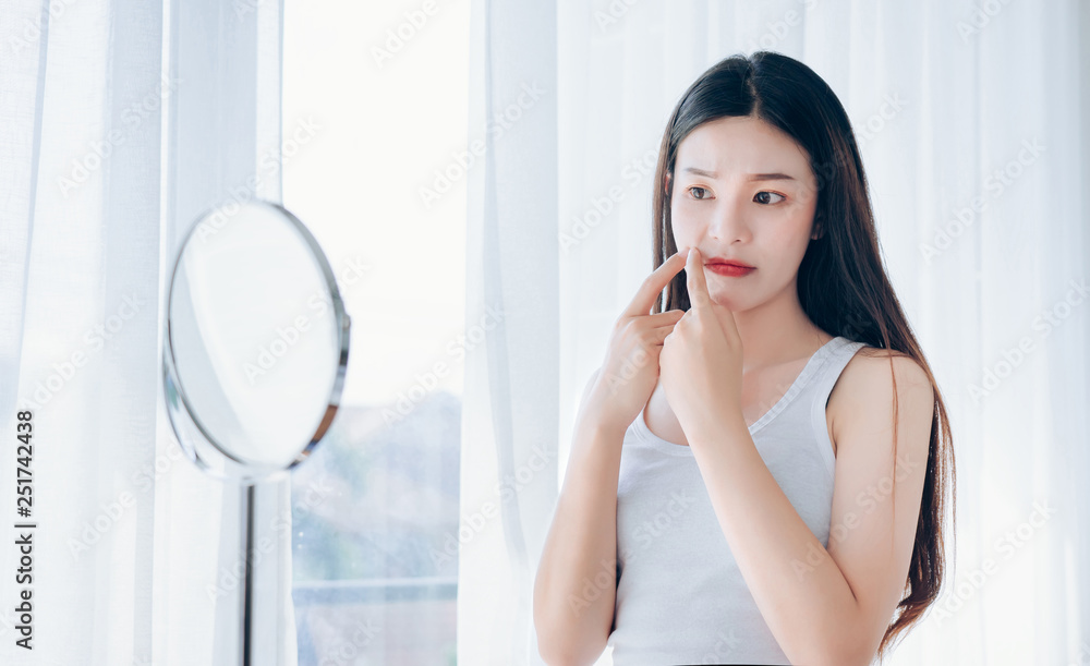 Young Asian woman squeeze acne problem face looking at mirror her without Skincare. Young Asian woman squeeze acne problem face looking at mirror her without Skincare.