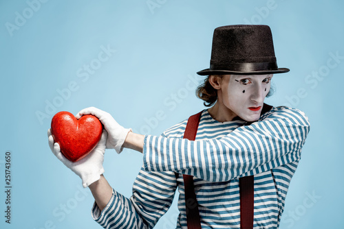 Portrait of an actor as a pantomime with white facial makeup posing with red heart on the blue background