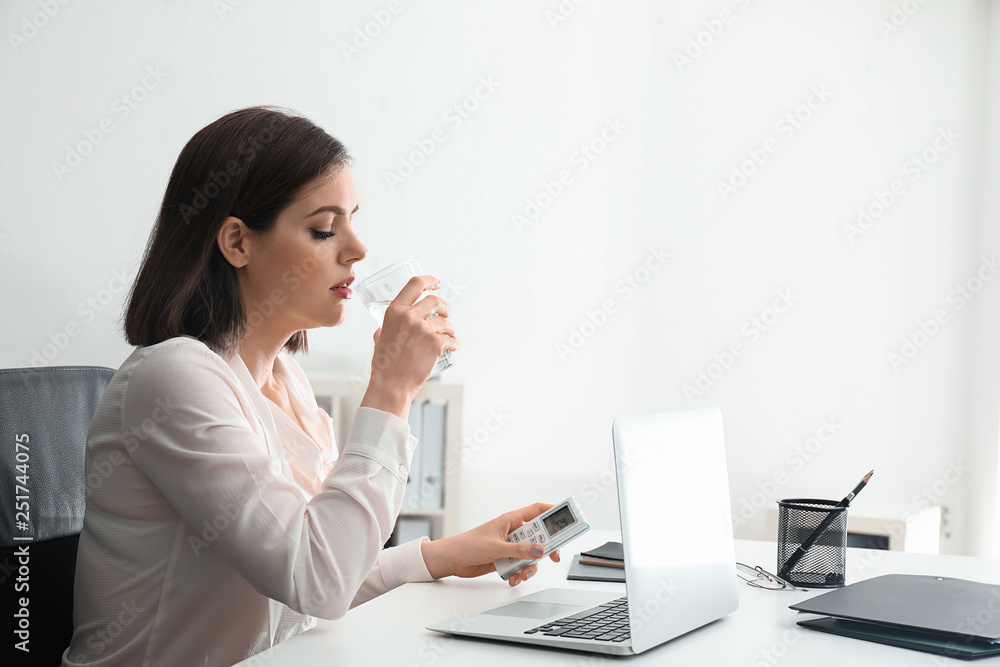 Young woman drinking water in office with operating air conditioner Young woman drinking water in office with operating air conditioner
