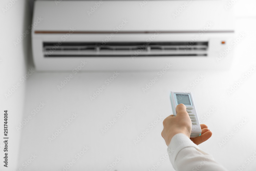 Young woman switching on air conditioner at home
