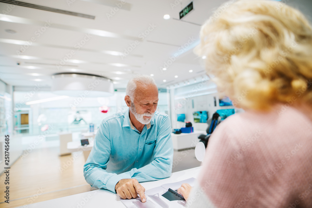 Grandparents looking at brochure and looking some products to buy while standing in tech store. Man pointing at product he like.