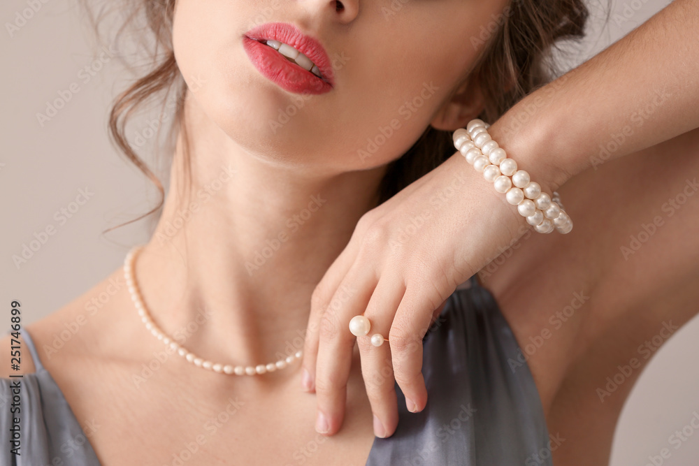 Young woman with beautiful pearl jewelry on light background, closeup