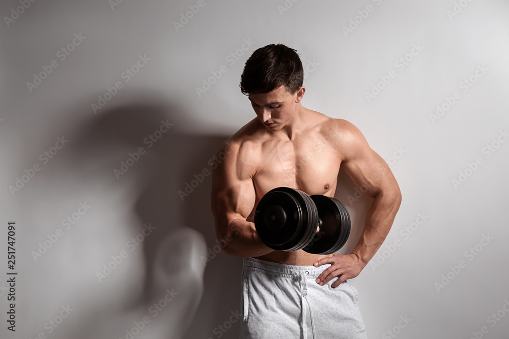 Muscular bodybuilder with dumbbell on light background Muscular bodybuilder with dumbbell on light background