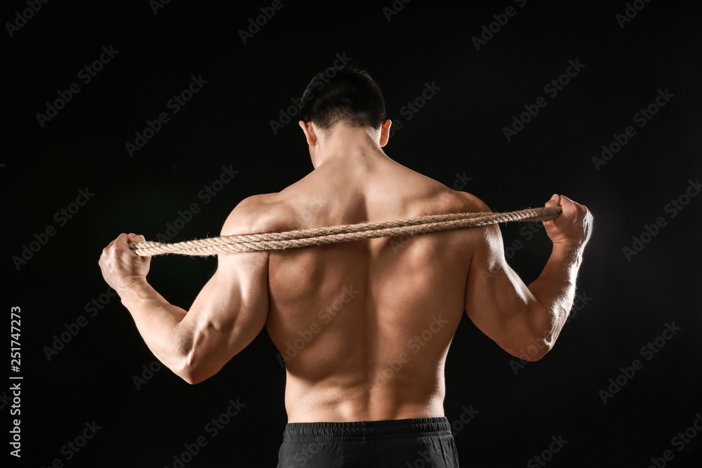 Muscular bodybuilder with rope on dark background, back view Muscular bodybuilder with rope on dark background, back view