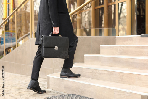 Businessman with stylish briefcase going upstairs outdoors photo