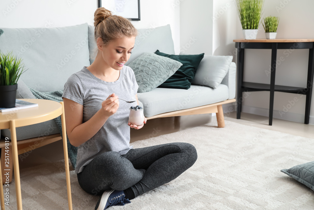 Sporty young woman eating tasty yogurt at home Sporty young woman eating tasty yogurt at home