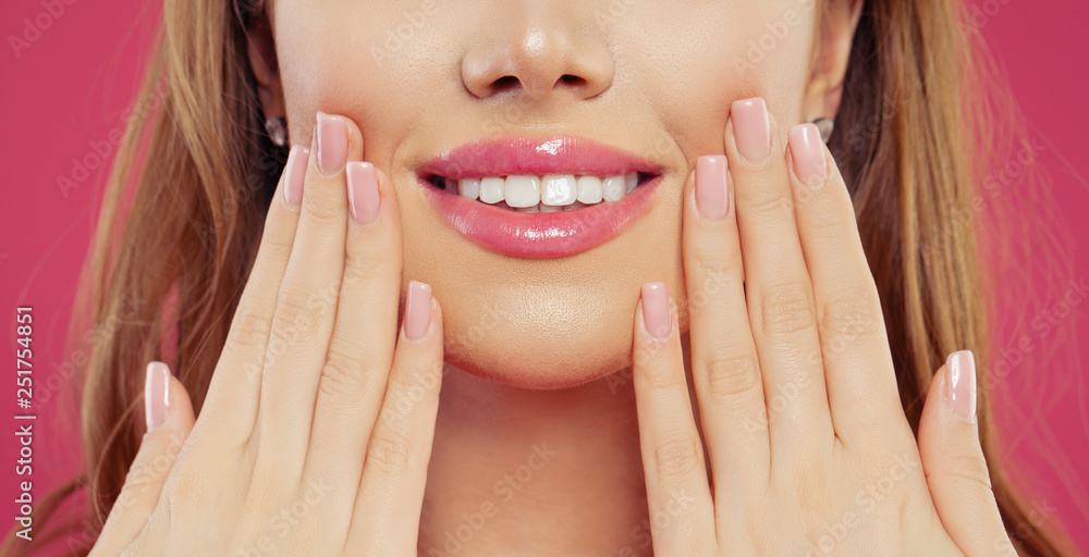 Fototapeta premium Beautiful woman smiling and showing her hand with manicure nails with natural pink nail polish. Makeup lips with pink color glossy lipstick