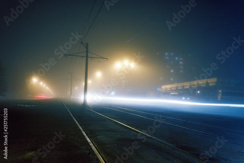 road with poles with high-voltage wires and tram tracks or tram rails , evening fog on the streets, poles with high-voltage wires, cityscape with freeze light or light painting