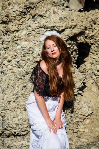 Portrait of young beautiful redhead woman in dress sitting on the rock