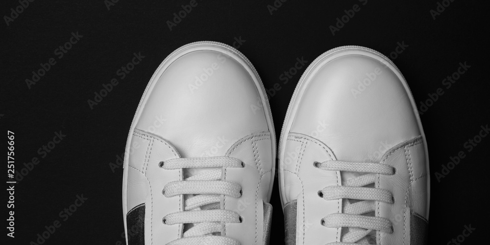 Overhead photo of female white sneakers on black background. Wide