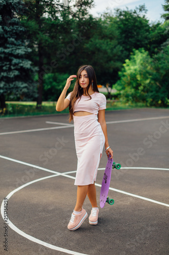 Portrait of a smiling charming brunette female holding her skateboard on a basketball court. © Smile