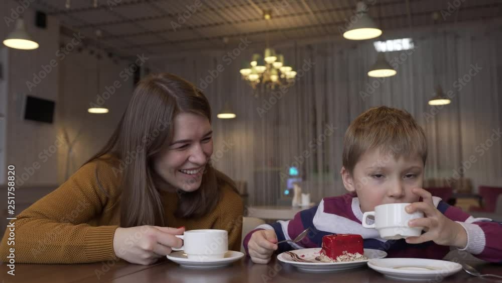 Funny Little Boy And Beautiful Young Mother Drink Tea And Eat Cake Funny Little Boy And Beautiful Young Mother Drink Tea And Eat Cake