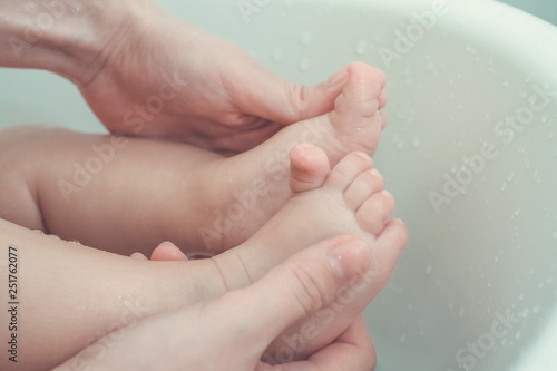 mother holding and massage baby's feet while taking a bath in bathtub. vintage photo and film style.