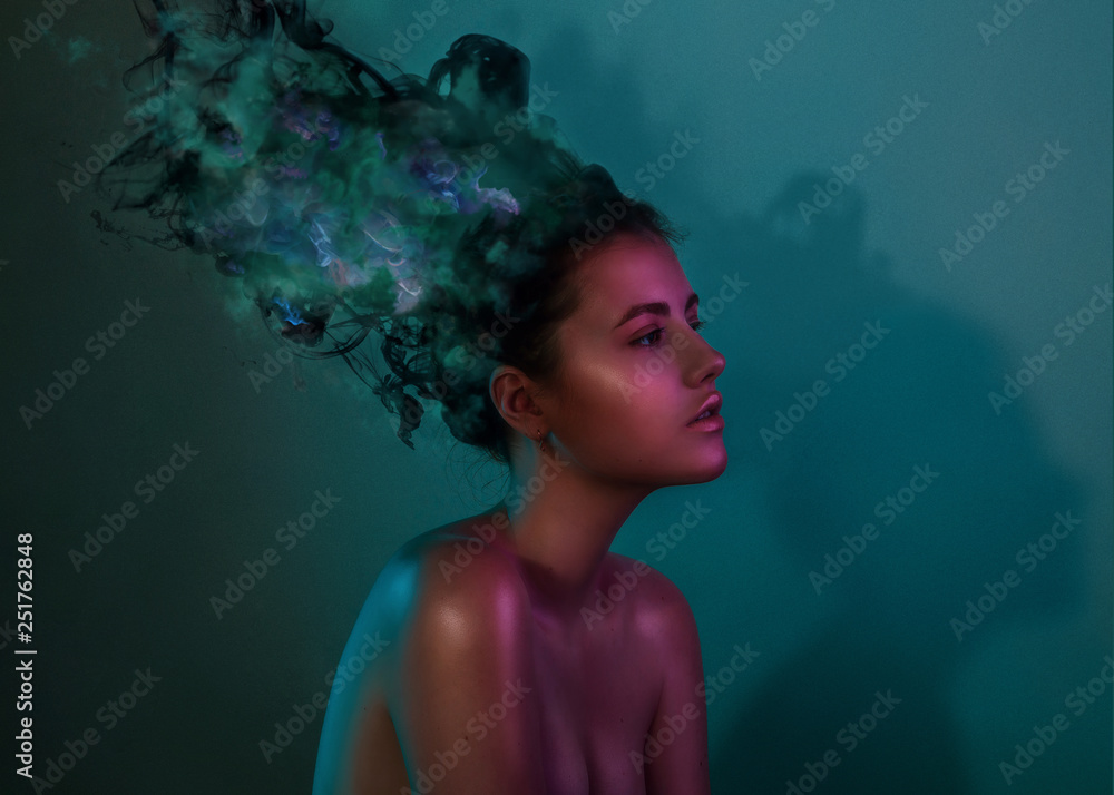Fashion trend portrait of young girl in studio with smoke color ink instead of hair. Light colored gels filters. Girl gloss face in blue and purple color light on dark blue background