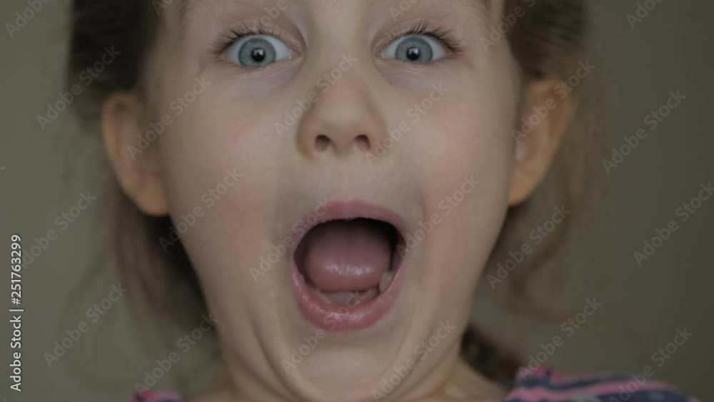 Girl looks and is surprised and happy to receive a surprise. Portrait little girl with blue eyes looking at camera. Closeup. Portrait of young child surprised and shocked . Close up. Girl looks and is surprised and happy to receive a surprise. Portrait little girl with blue eyes looking at camera. Closeup. Portrait of young child surprised and shocked . Close up.