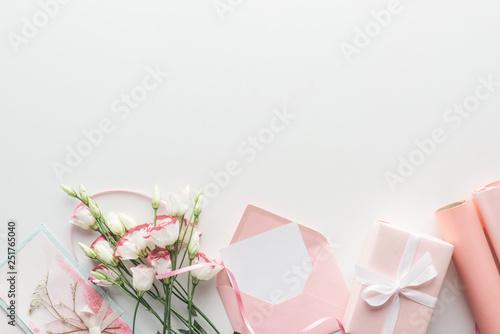 top view of pink eustoma, rolls of paper, wrapped gifts, envelope and greeting card on grey background